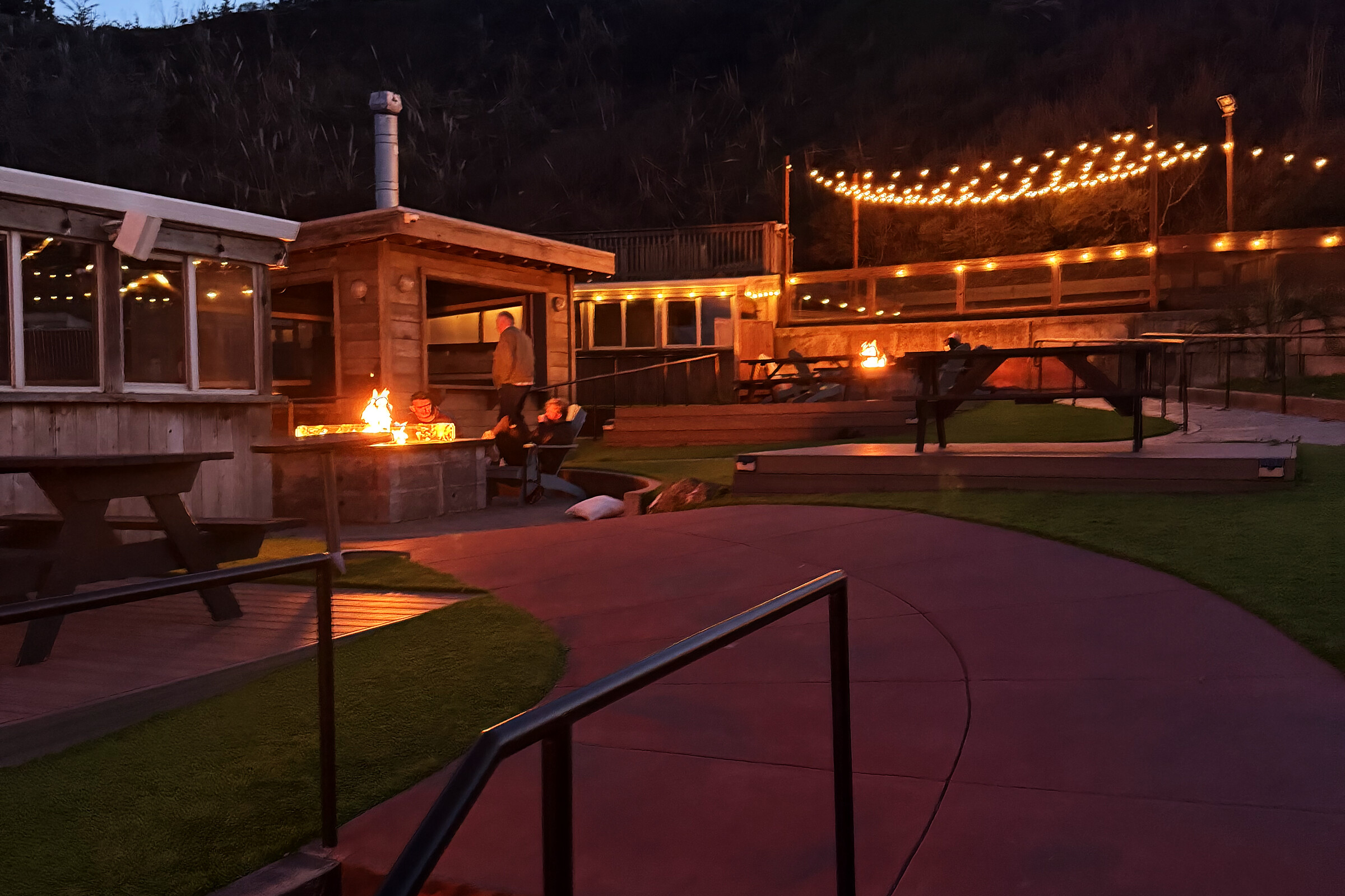 Rockaway Beach Brewery beer garden at dusk with string lights and fire pits